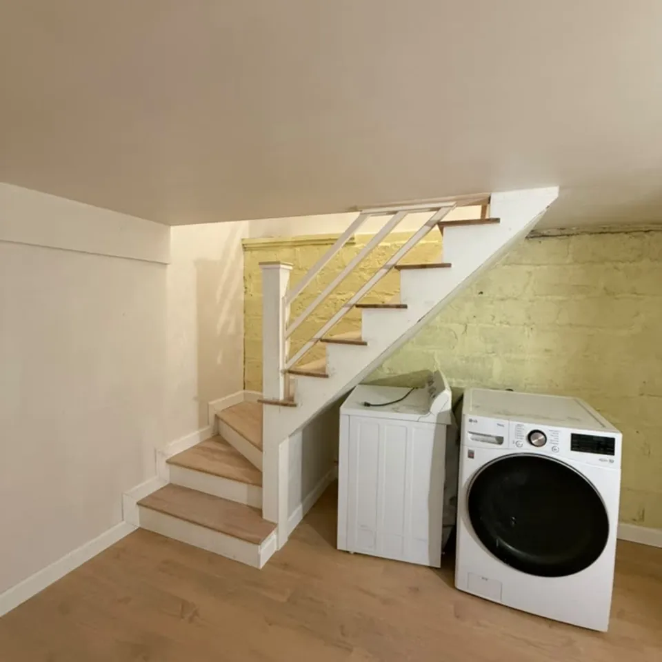 After: the same Arlington, MA basement with rebuilt stairs, vinyl plank floor and a finished laundry area by Innov Builders